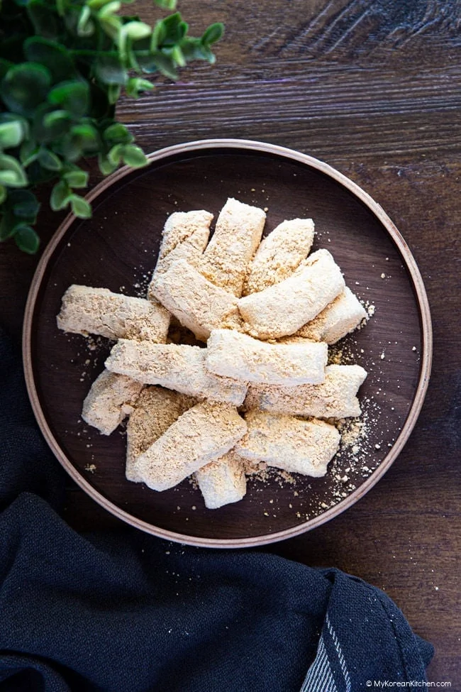 Petits morceaux de gâteau de riz coréen Injeolmi enrobés de poudre de soja sur une assiette en bois