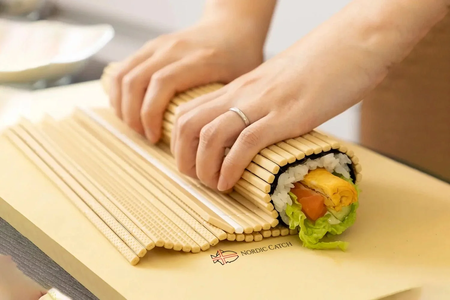 Main roulant un maki sushi avec une natte en bambou recouverte de film plastique