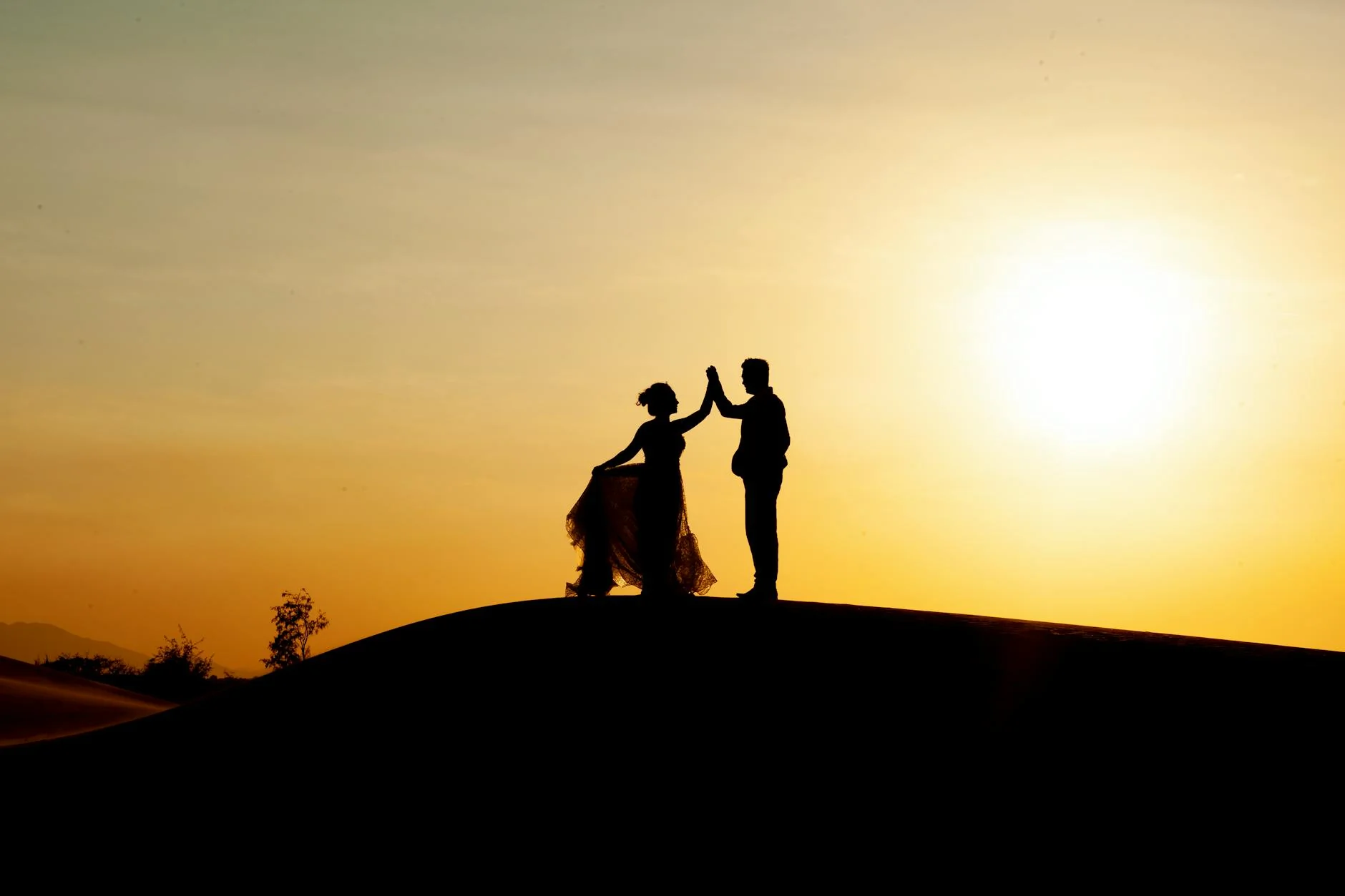 Silhouette d'un jeune couple se tenant la main devant un coucher de soleil
