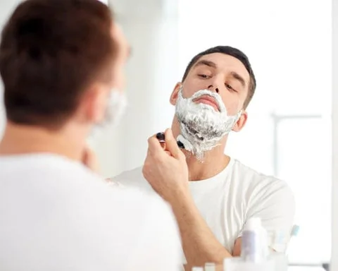 Homme se rasant le visage, illustrant le stress mécanique subi par la peau masculine