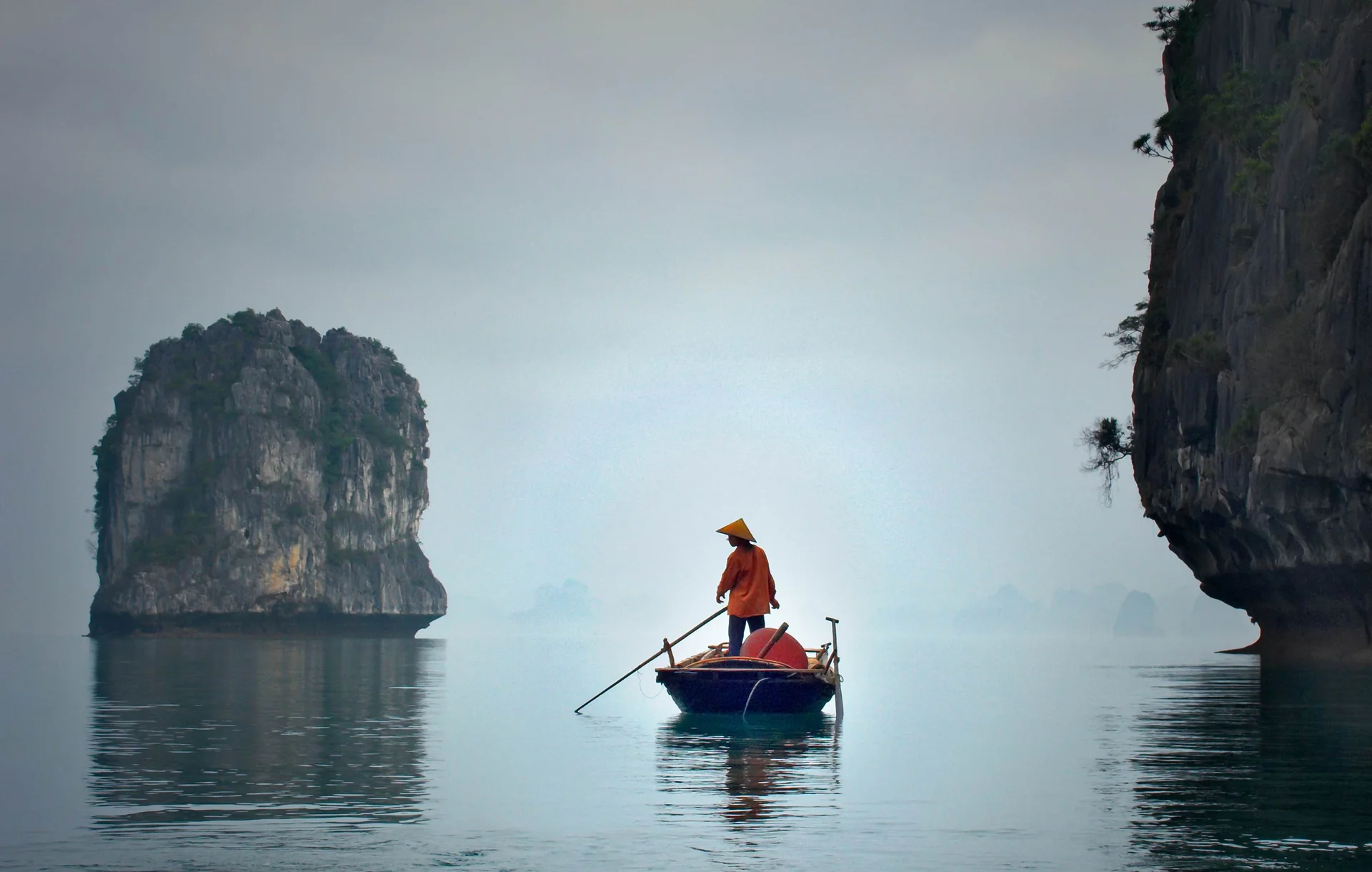 Pêcheur naviguant dans la brume matinale au milieu des pitons karstiques de la baie d'Ha Long