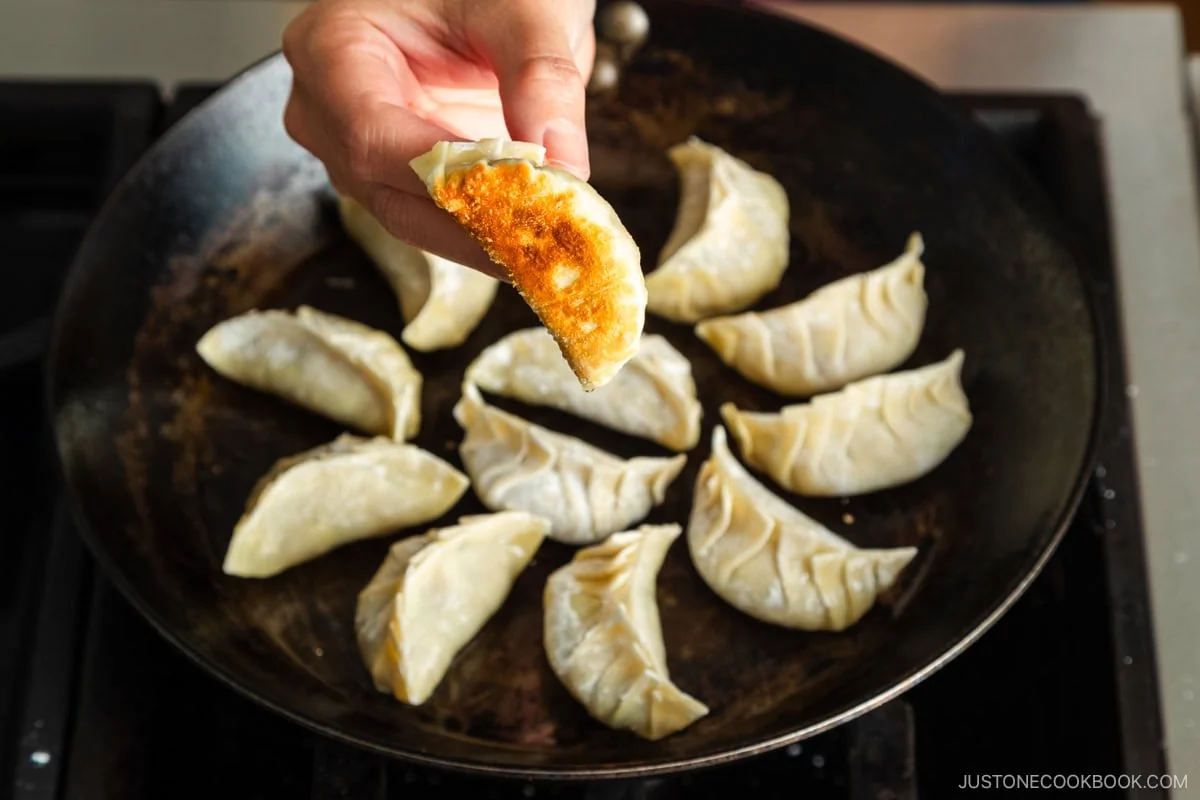 Gyoza en train de cuire dans une poêle, montrant une base parfaitement dorée