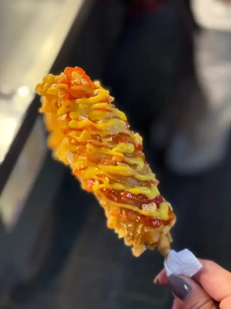 Un corn dog coréen frit recouvert de cubes de pommes de terre avec du fromage fondu